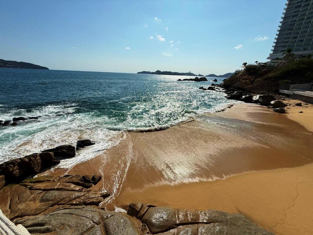 a beach with rocks and water and a building at Torres Gemelas Acapulco Suites in Acapulco