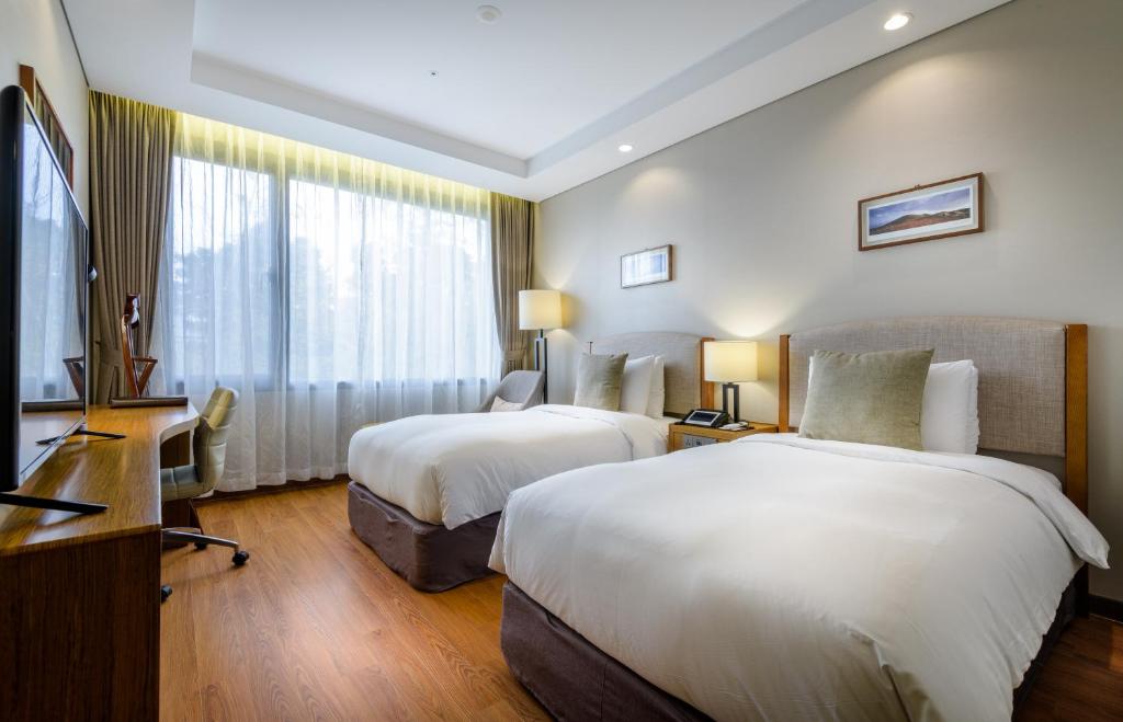 a hotel room with two beds and a desk at Parksunshine Jeju in Seogwipo
