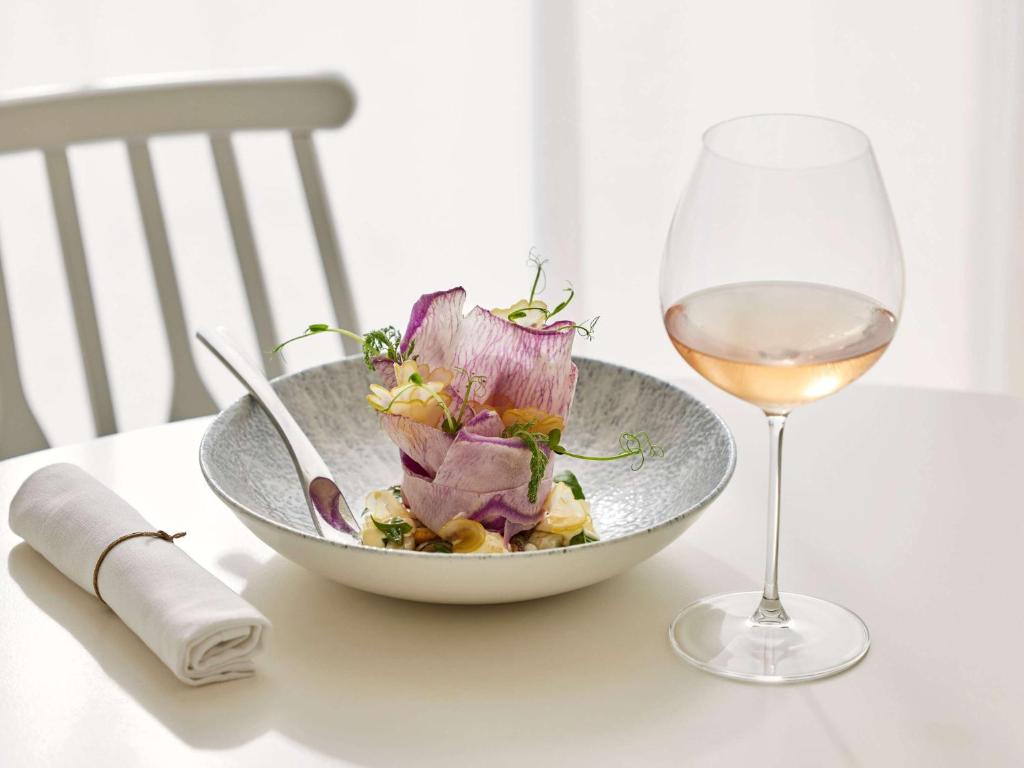a bowl of salad and a glass of wine on a table at Sofitel Golfe d'Ajaccio Thalassa Sea & Spa in Ajaccio