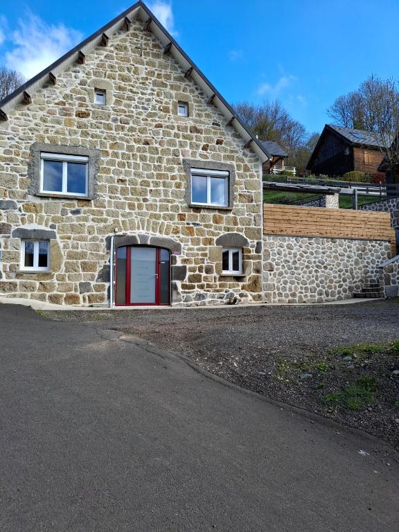 une maison en pierre avec une porte rouge et un mur en pierre dans l'établissement Les Roses Des Bois, à Murat-le-Quaire