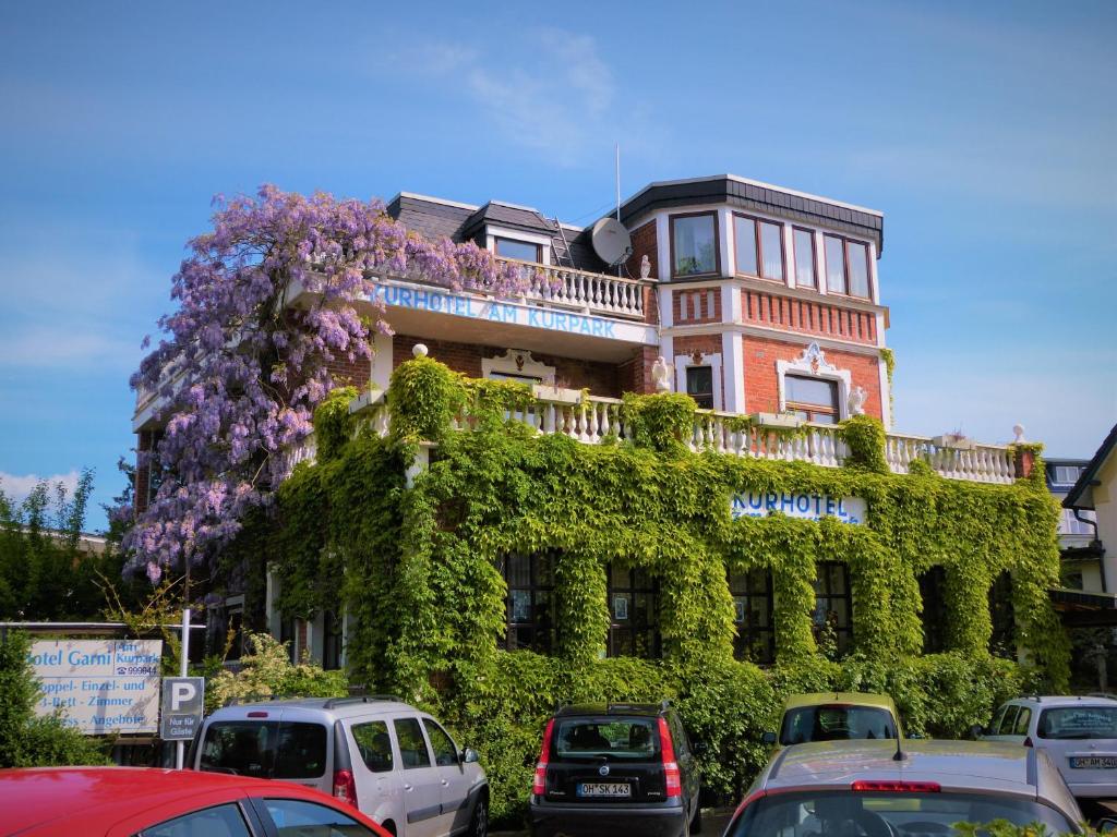 ein von Efeu bedecktes Gebäude mit Autos, die vorne geparkt sind in der Unterkunft Hotel Am Kurpark in Malente