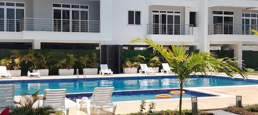 a swimming pool with white chairs and a building at Romi Homes in Mombasa