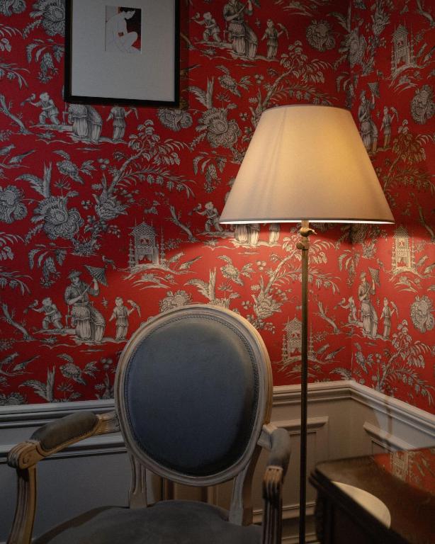 une lampe et une chaise dans une pièce avec du papier peint rouge dans l'établissement Hôtel De Buci, à Paris