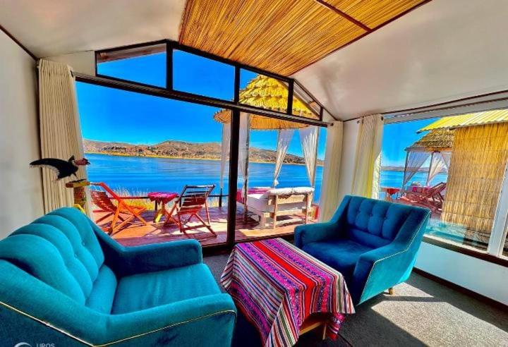 a living room with blue chairs and a view of the water at Titicaca posada del sol lodge in Puno