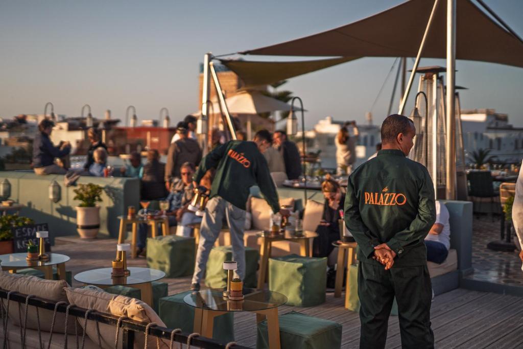 a group of men standing on a rooftop with tables and people at Le Palazzo in Essaouira