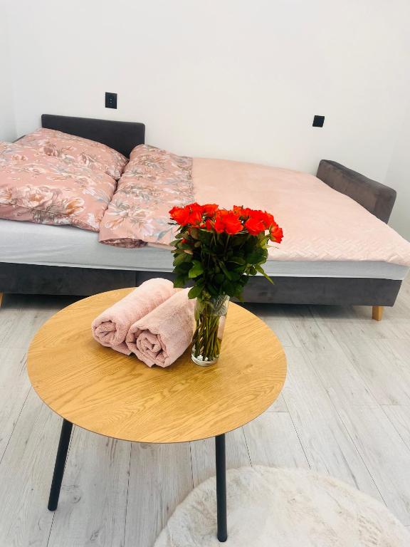 a table with a vase of red flowers on a bed at Zakątek Centrum in Suwałki