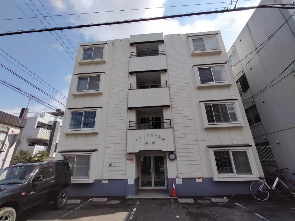 a white building with a car parked in front of it at アンブローシア平岸 in Toyohira