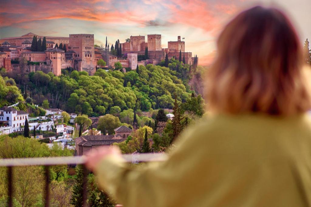 a woman standing on a balcony looking at a castle at Cueva la Bonica - Hostatel in Granada