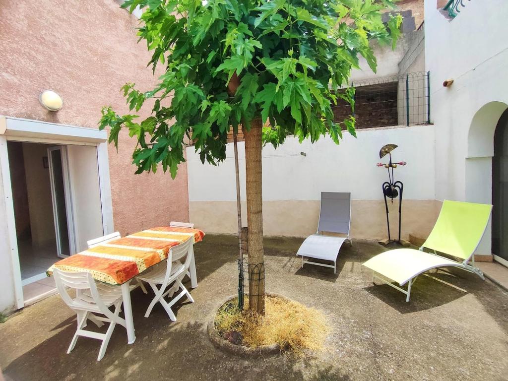 une table, des chaises et un arbre dans une cour dans l'établissement Havre de paix au cœur du village de Florensac., à Florensac