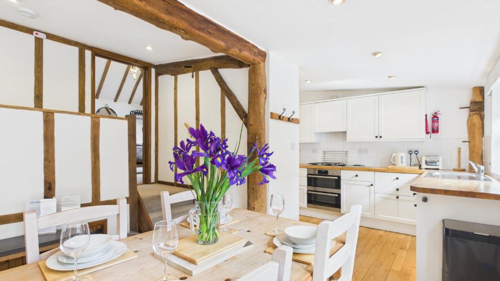 a kitchen and dining room with a wooden table with purple flowers at The Cote is a stunning rural barn beach 3 miles in Haven Street