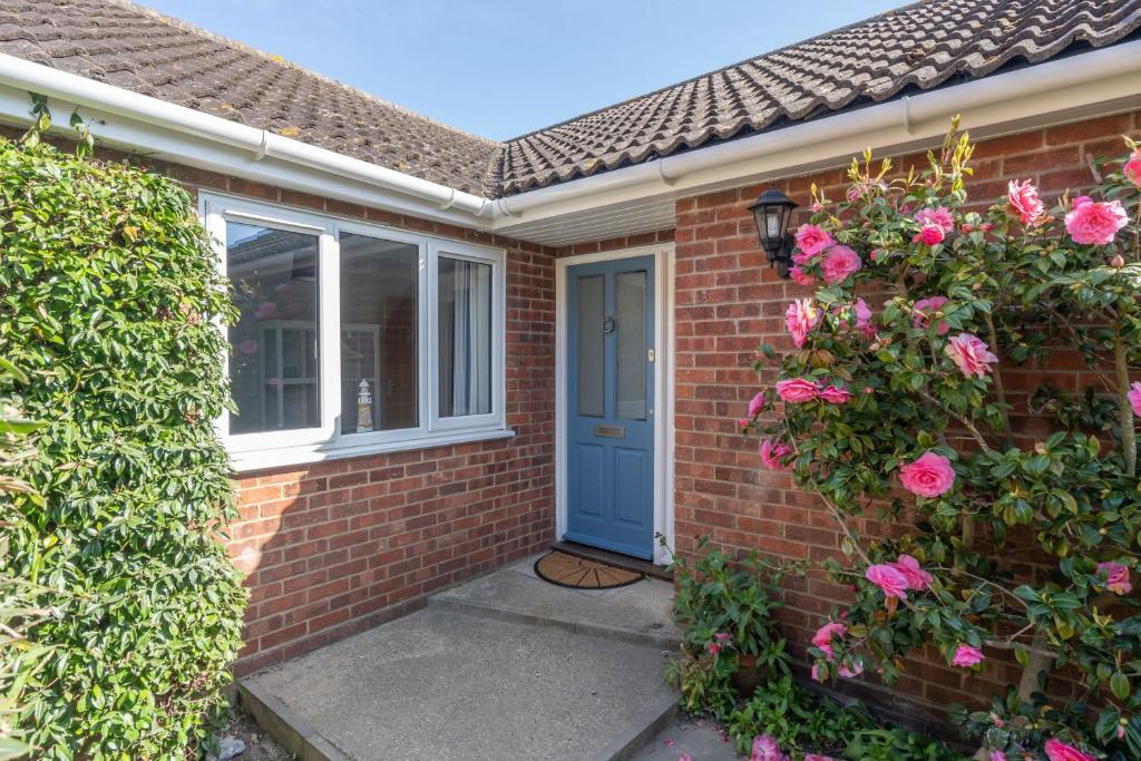 a brick house with a blue door and pink roses at Cobbles End by Winterton Cottages in Winterton-on-Sea