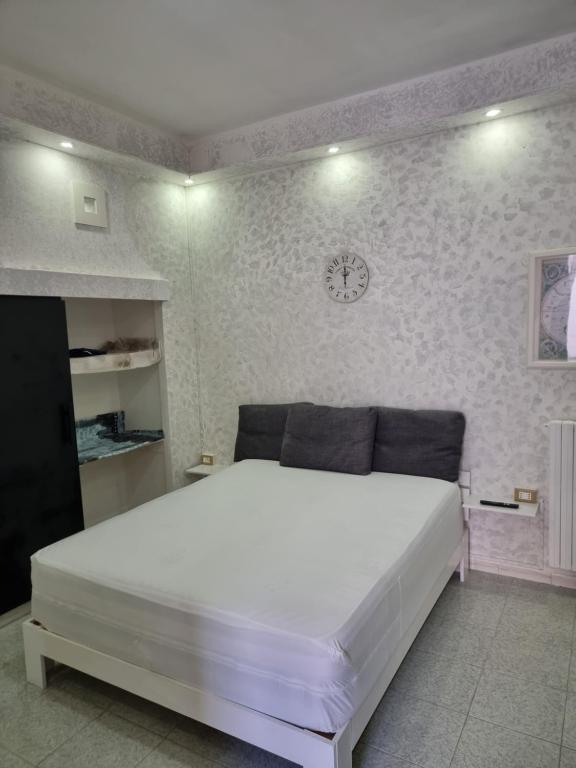 ein weißes Bett in einem Schlafzimmer mit einer Uhr an der Wand in der Unterkunft Vieste Holiday Homes - Appartamento Vacanze Centro Luxury con balcone a pochi passi dal mare in Vieste