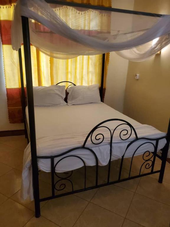a bed with a black frame and white sheets at 2M Tarangire Lodge in Kwa Kuchinia