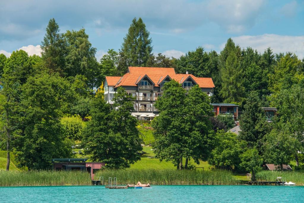 ein großes Haus am Ufer eines Sees in der Unterkunft Kleines Hotel Kärnten in Egg am Faaker See