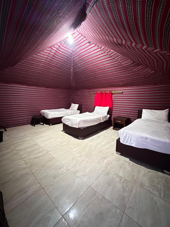Habitación con 3 camas y pared roja. en Desert Star Camp, en Wadi Rum