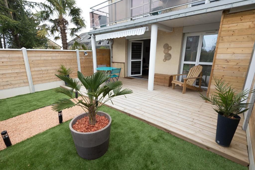 une terrasse en bois avec deux palmiers dans une cour dans l'établissement Bel appart près du port et de la plage, à Courseulles-sur-Mer