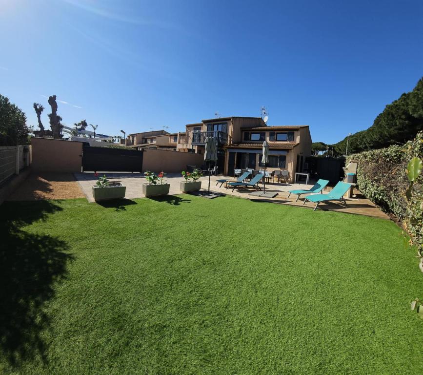 une cour avec de l'herbe verte et une maison dans l'établissement Maison tout confort 4 ch 8p domaine privé avec piscines, et plage à 10 min à pied, à Portiragnes