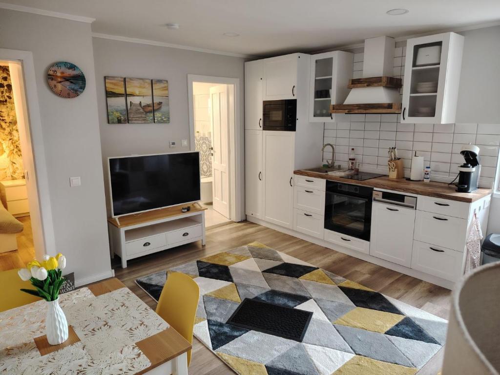 una cucina con armadi bianchi, TV e tavolo di Pupi Apartmanház a Balatonlelle