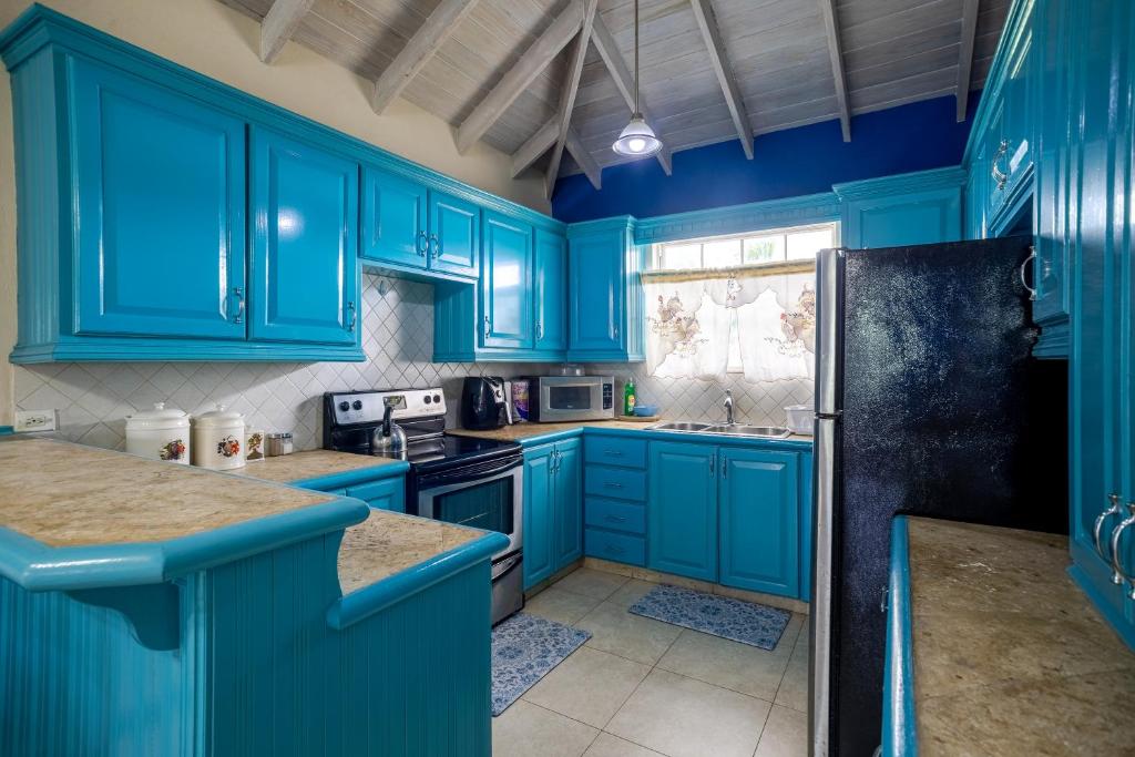 een blauwe keuken met blauwe kasten en een zwarte koelkast bij Best E Villas Providence Ch Ch in Christ Church
