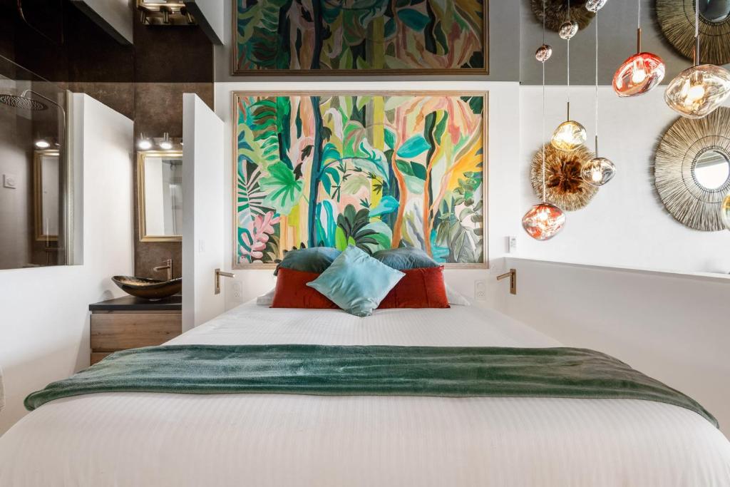 une chambre avec un grand lit blanc avec des œuvres d'art colorées sur le mur dans l'établissement Téquila - Heliopolis AB, au Cap d'Agde