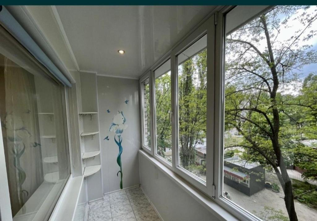 ein Zimmer mit zwei Fenstern mit Blick auf einen Baum in der Unterkunft Просторная квартира, Калиновая 66, левый берег in Nizhnedneprovsk