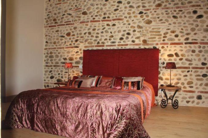 um quarto com uma cama grande e uma parede de tijolos em Terre de Garance em Lagardelle-sur-Lèze