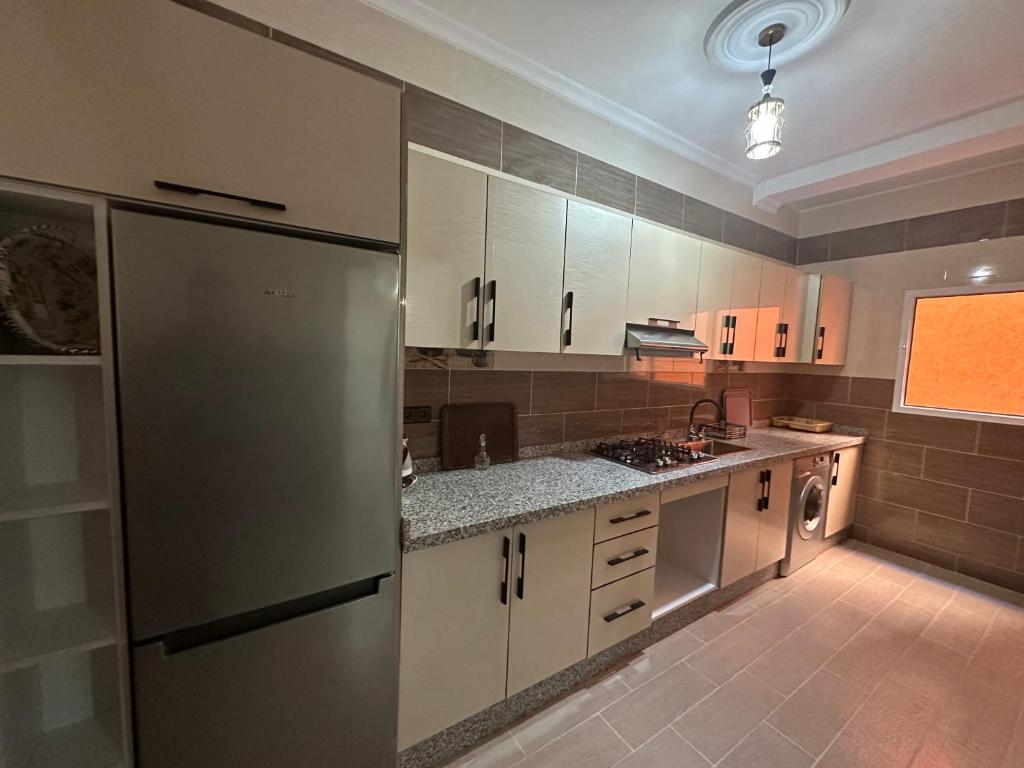 a kitchen with white cabinets and a stainless steel refrigerator at Appartement à Houma, proche Port Tanger Med in Dalia