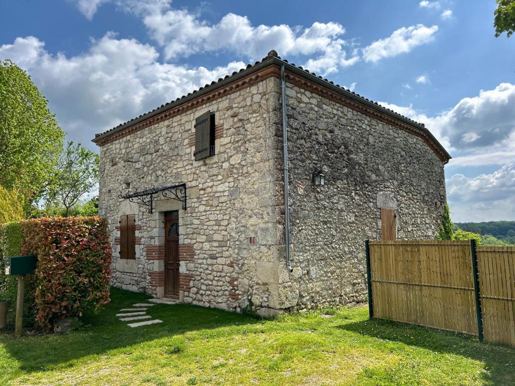 un ancien bâtiment en pierre avec une clôture en bois dans l'établissement Maison en pierre cosy avec piscine privé, à Dolmayrac