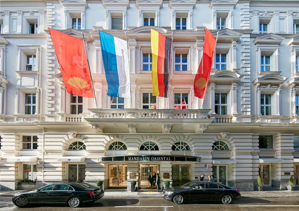 deux voitures garées devant un bâtiment arborant des drapeaux dans l'établissement Mandarin Oriental, Munich - Germany's Best City Hotel 2024, à Munich