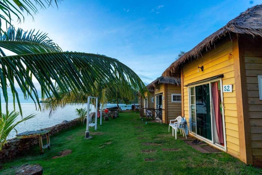 a yellow house with a grass roof next to the water at kohchang7seaview Bungalows in Ban Bang Bao