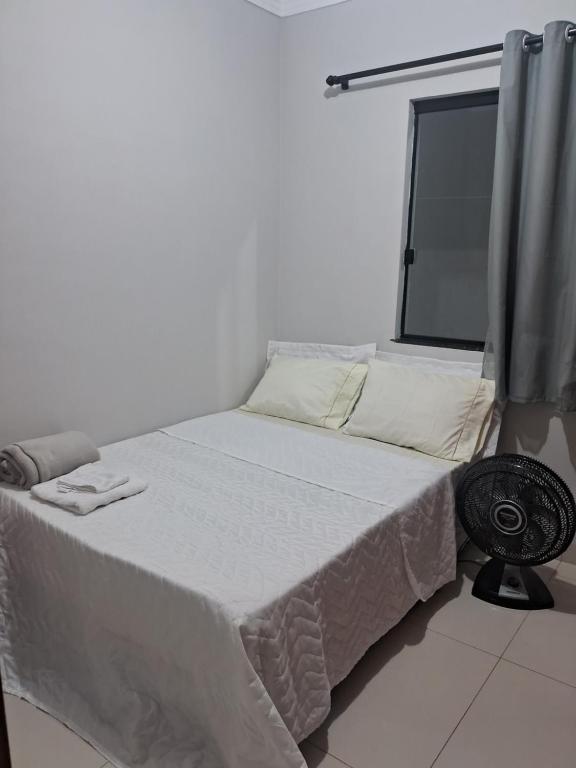Un dormitorio blanco con una cama con ventana. en Quarto da Tay, en Paranavaí