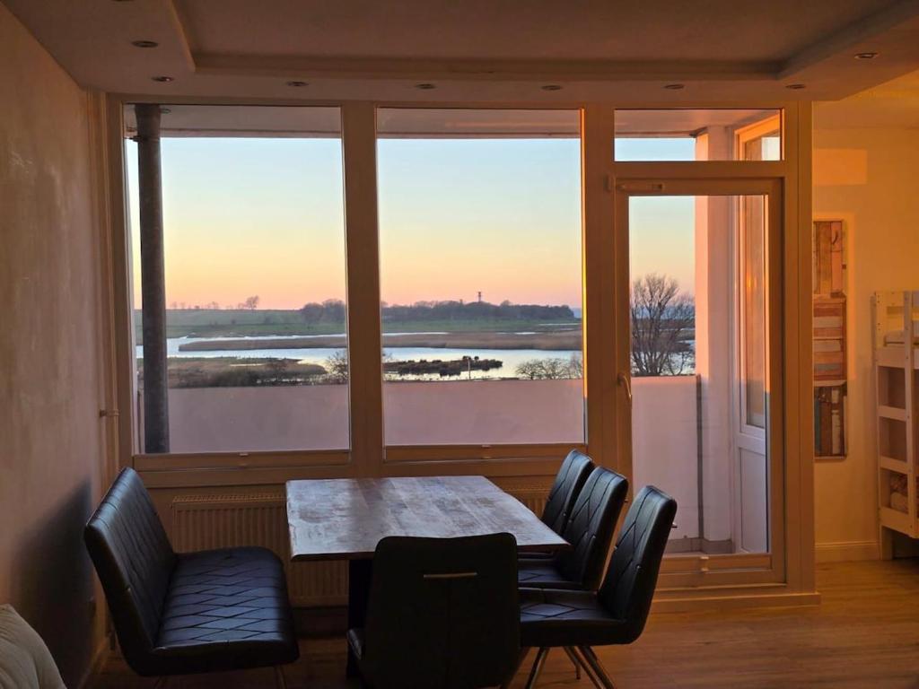 a table and chairs in a room with a large window at Moderne Wohnung mit Sonnenuntergang über dem Meer in Heiligenhafen