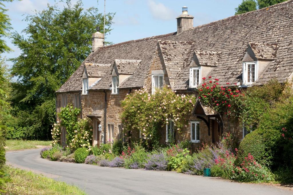 an old stone house with flowers on the side of a road at The Old Post Office - Adlestrop in Adlestrop