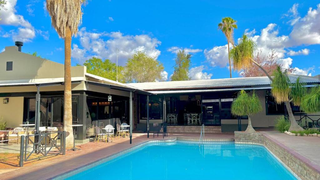 a swimming pool in front of a house with palm trees at Auob Country Lodge in Gochas