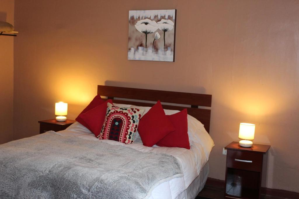 a bedroom with a bed with red pillows and two lights at Casa En La Precordillera in San José de Maipo