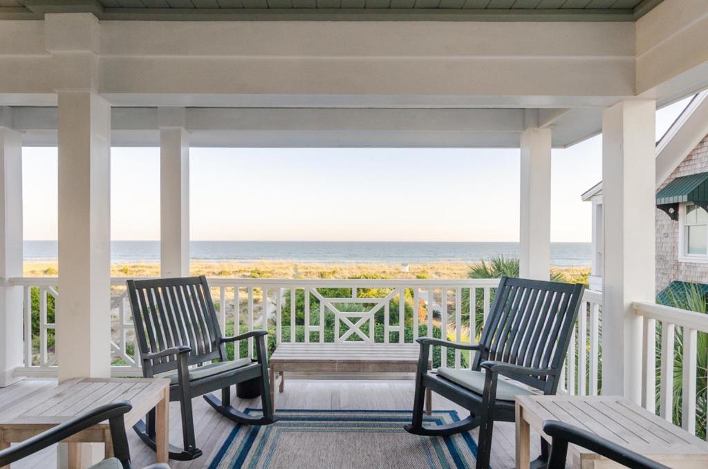 a porch with chairs and a table and the ocean at Blake Cottage by Bryant Real Estate in Wrightsville Beach
