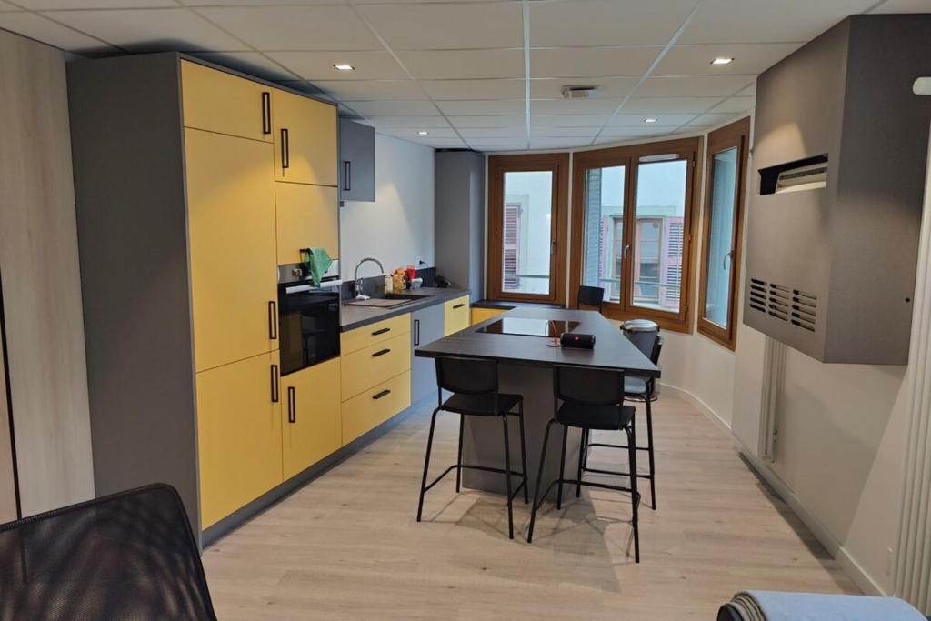 une cuisine avec des placards jaunes, une table et des tabourets dans l'établissement Appartement Moderne au Cœur de Chambéry, à Chambéry