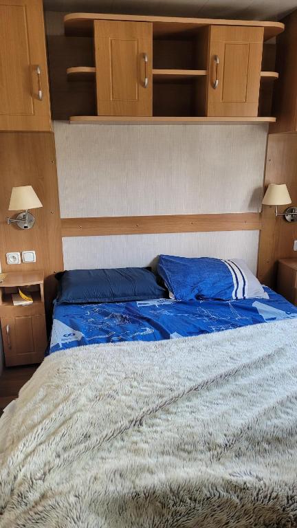 a bed with blue pillows on it in a room at Joli Mobilhome 4 personnes proche Mimizan océan et lac in Sainte-Eulalie-en-Born