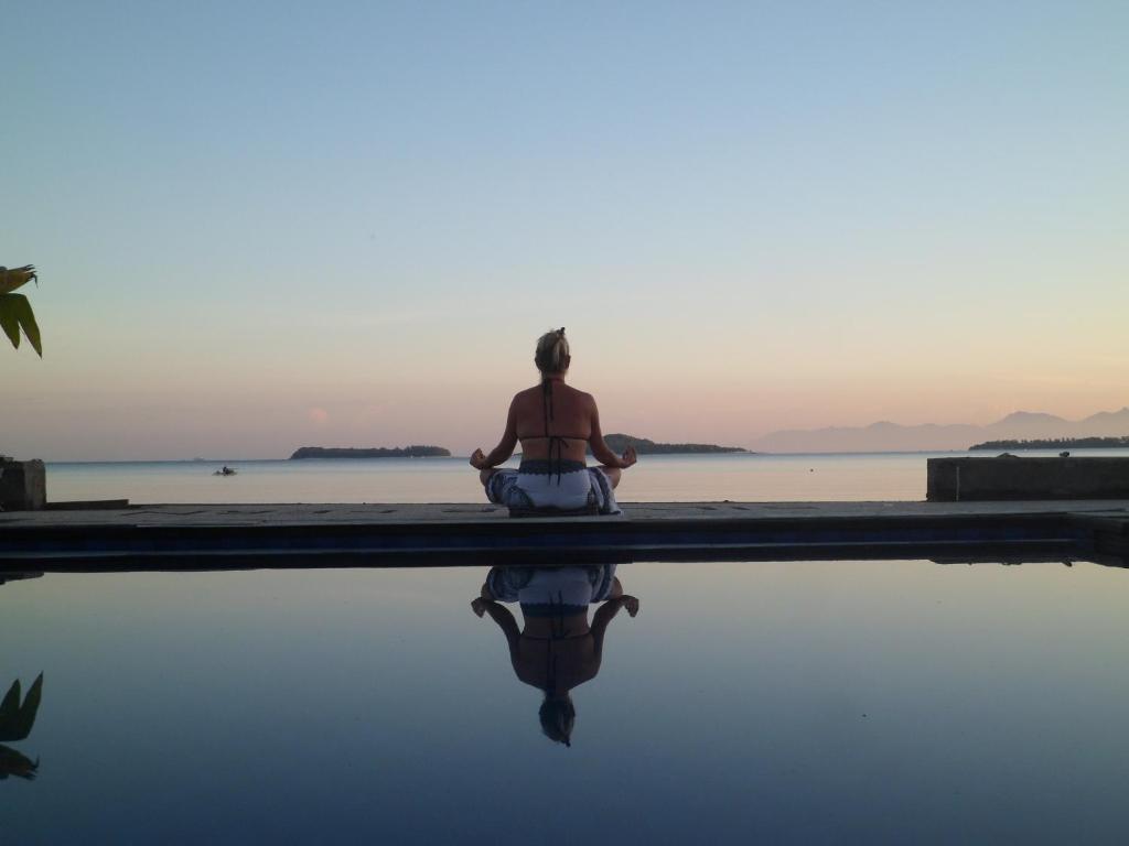 Una donna seduta in una posa meditativa vicino a una piscina di Silver Fern Beach Retreat a Sekotong