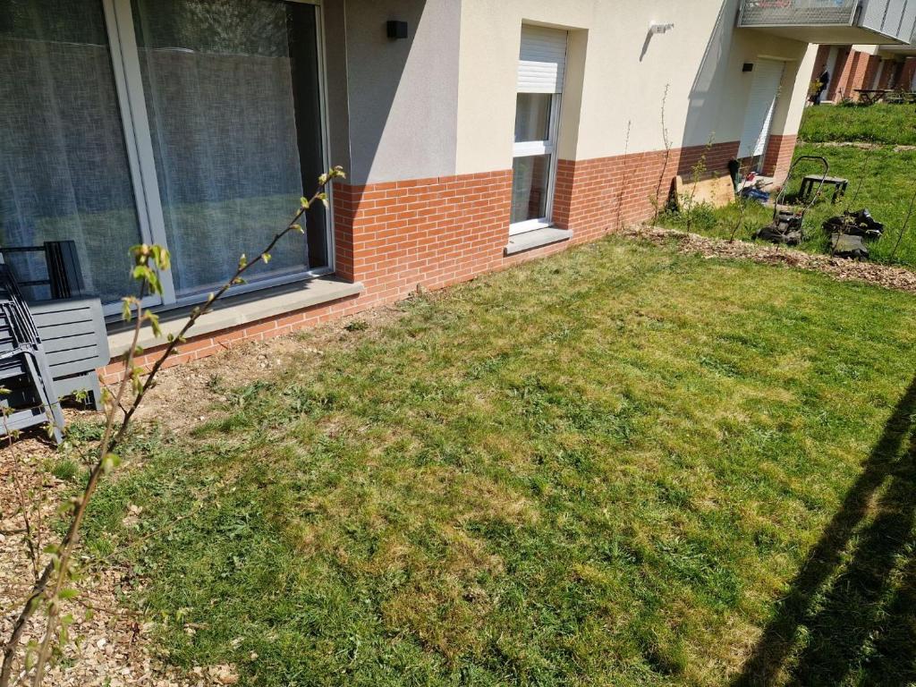 ein Hof eines Hauses mit einem Rasen mit einer Bank in der Unterkunft Le Cocon Urbain in Amiens