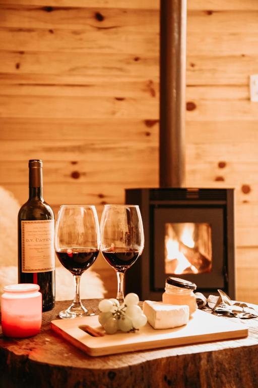two glasses of wine and cheese on a table with a fireplace at Chalés Bosque das Oliveiras in Urubici