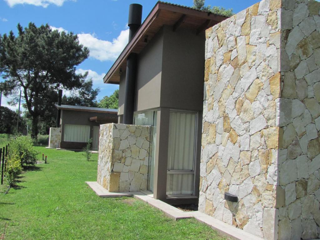 a house with a stone wall next to a yard at Complejo Aires del Bosque in Chascomús
