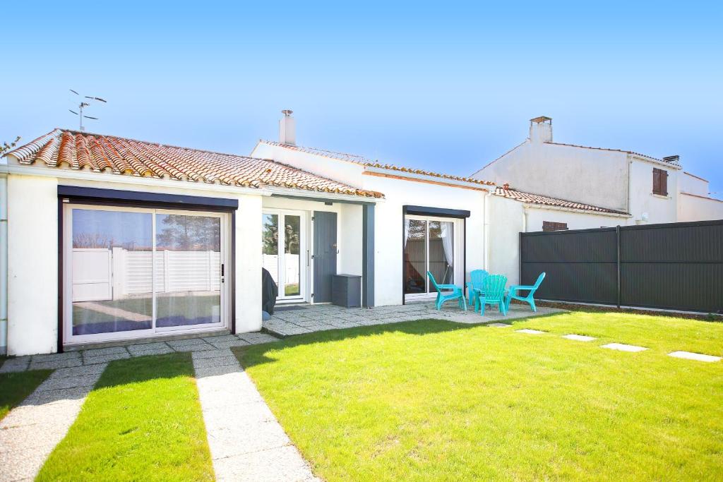 une maison blanche avec une cour dotée de 2 chaises bleues dans l'établissement Le Murmure des Vagues - Proche plage, à La Tranche-sur-Mer
