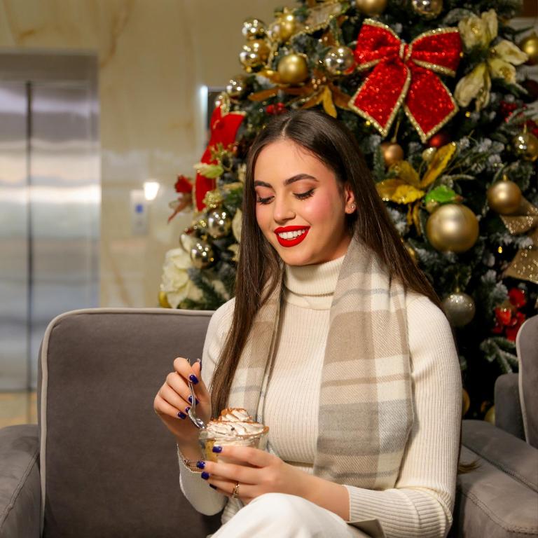 a woman sitting on a couch in front of a christmas tree at Doanesia Premium Hotel & Spa in Tirana