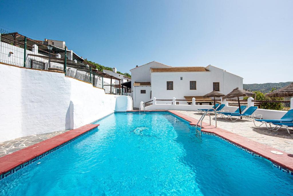 a swimming pool with blue chairs and a house at El Pajar in Málaga