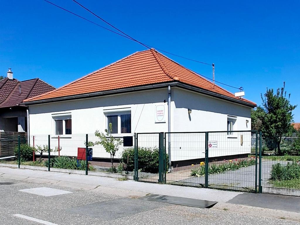 a white house with an orange roof behind a fence at SZEDERMÁLNA Vendégház in Sárospatak