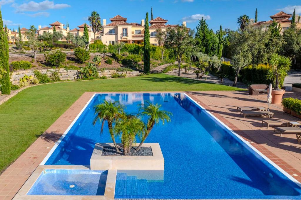 una piscina con palmeras junto a una casa en Monte Rei 2 bed linked villa, en Vila Nova de Cacela