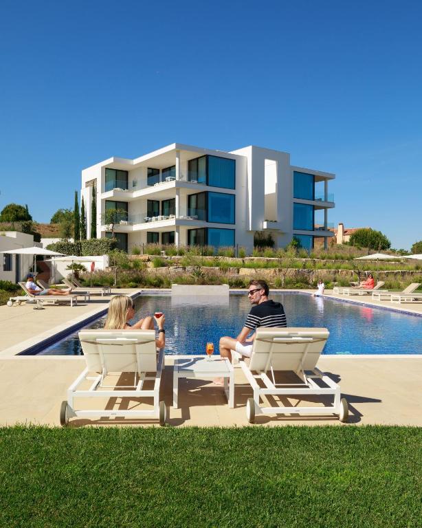 a man and woman sitting in lounge chairs next to a pool at Monte Rei 3 bed Penthouse Apt in Vila Nova De Cacela