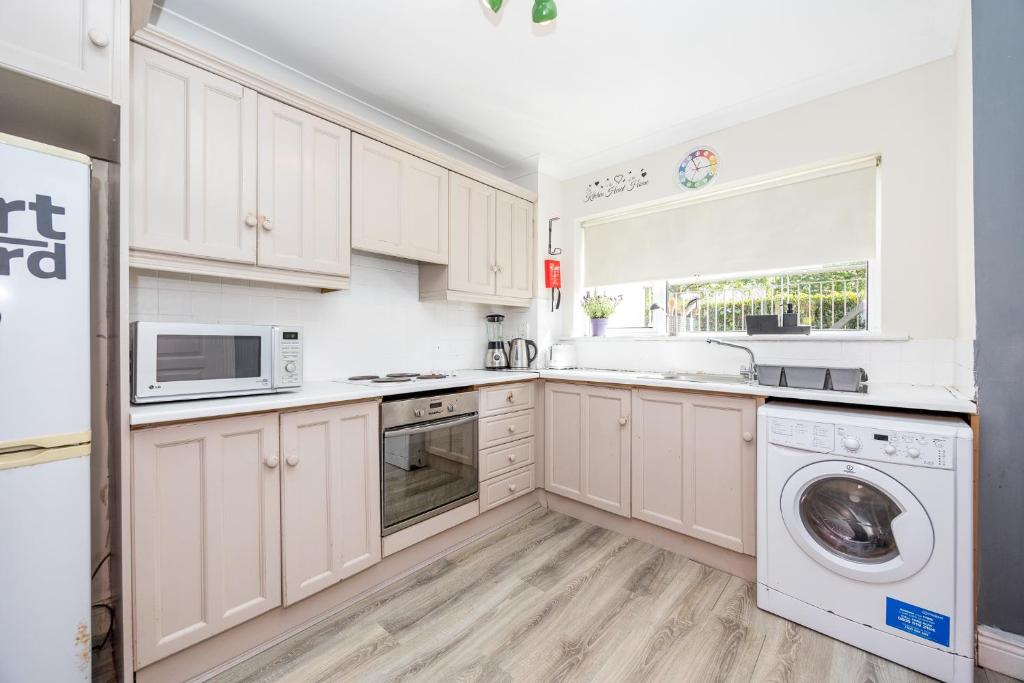 a kitchen with white cabinets and a washer and dryer at Cosy 2-Bedroom Apartment near Airport in Dublin