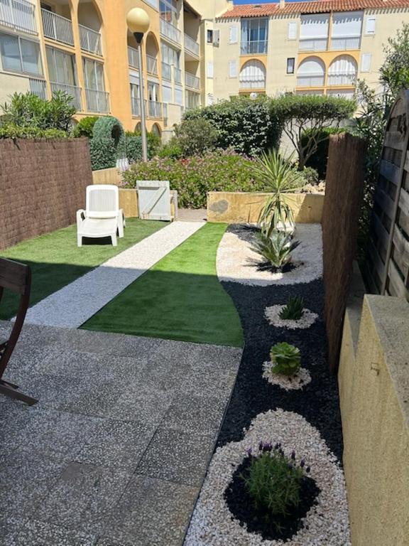 un jardin avec un banc et une chaise dans un bâtiment dans l'établissement Appartement T2 avec son rez de jardin de 40 m2 5 couchages 250m de la plage et 15km de l'Arena, à Narbonne-Plage
